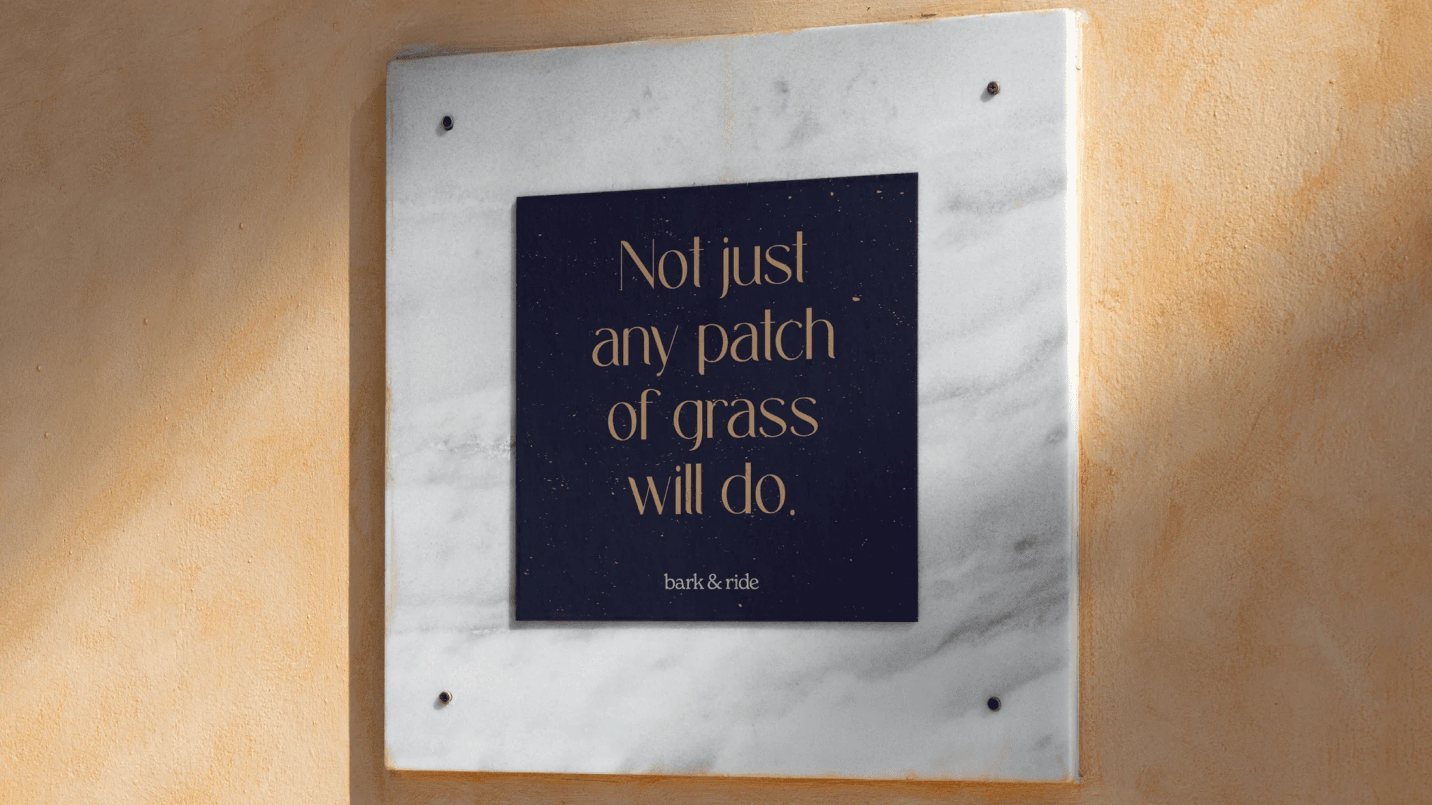 A navy plaque mounted on marble reading “Not just any patch of grass will do.” above the bark & ride wordmark