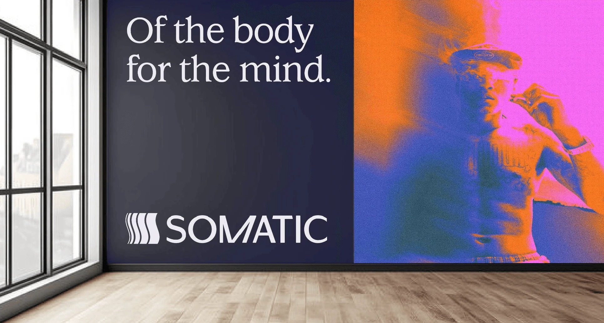 A wall-sized Somatic mural in a daylit room: the line “Of the body for the mind.” beside a thermal-toned portrait in magenta and orange