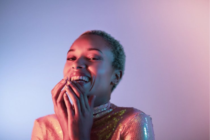 A laughing woman in sequins, lit pink and blue